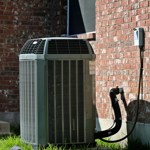 Outdoor AC condenser on the grass beside a red brick home with its electrical disconnect