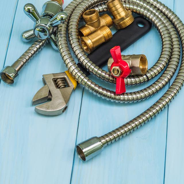Braided steel supply hoses, brass fittings, a shutoff valve, and a wrench on a blue wood surface