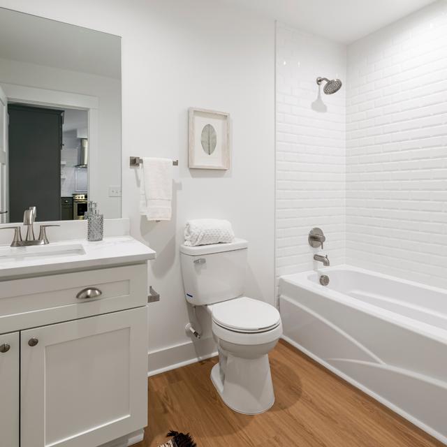 Bright white bathroom with a toilet, vanity, and tub with a tiled shower surround