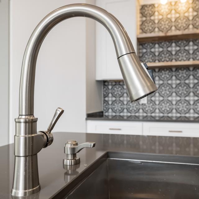 Brushed nickel pull-down faucet over a dark kitchen sink with a tile backsplash