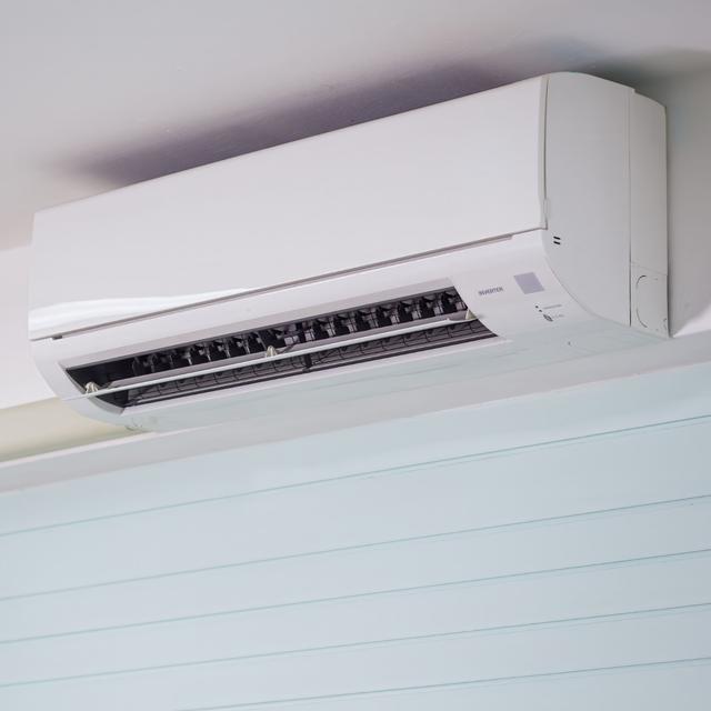 White ductless mini split head mounted high on a light blue wall