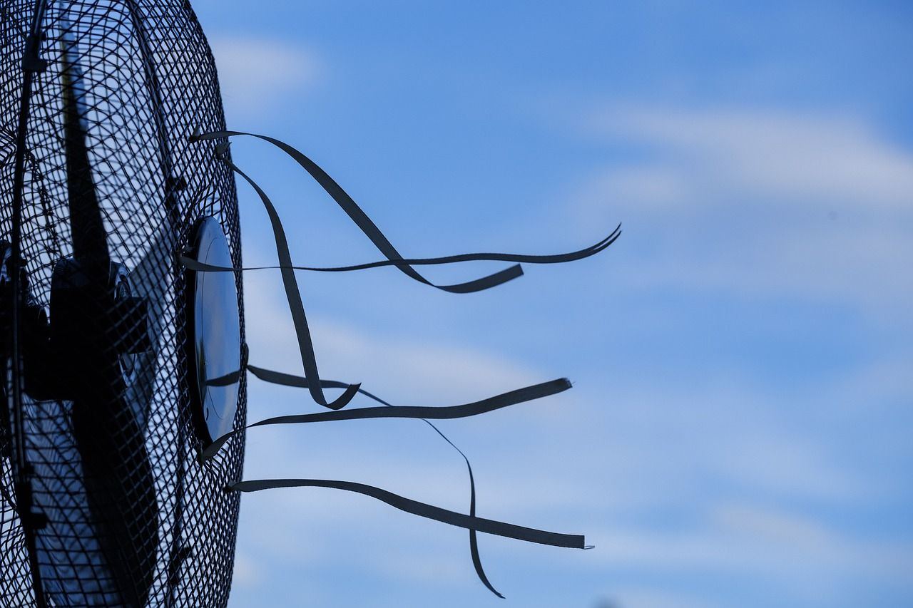 Electric fan with ribbons streaming from its grille against a blue summer sky