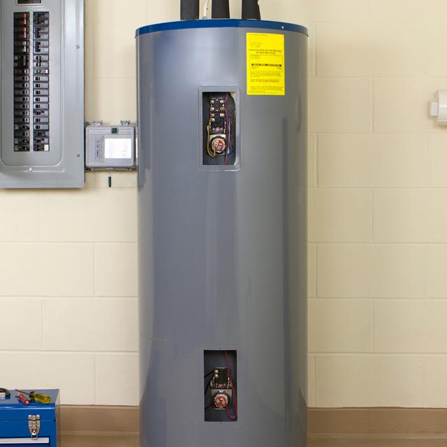 Electric water heater with both access panels open, showing the thermostats and heating elements, next to a breaker panel