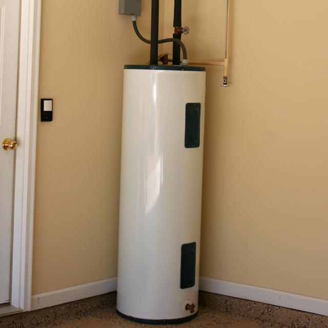 White electric tank water heater installed in the corner of a garage beside a door