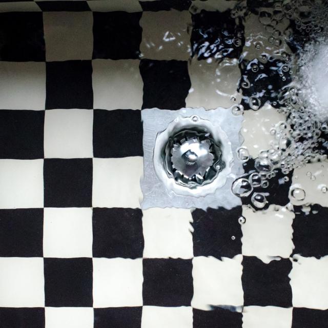 Water pooling around a floor drain on black and white checkered tile
