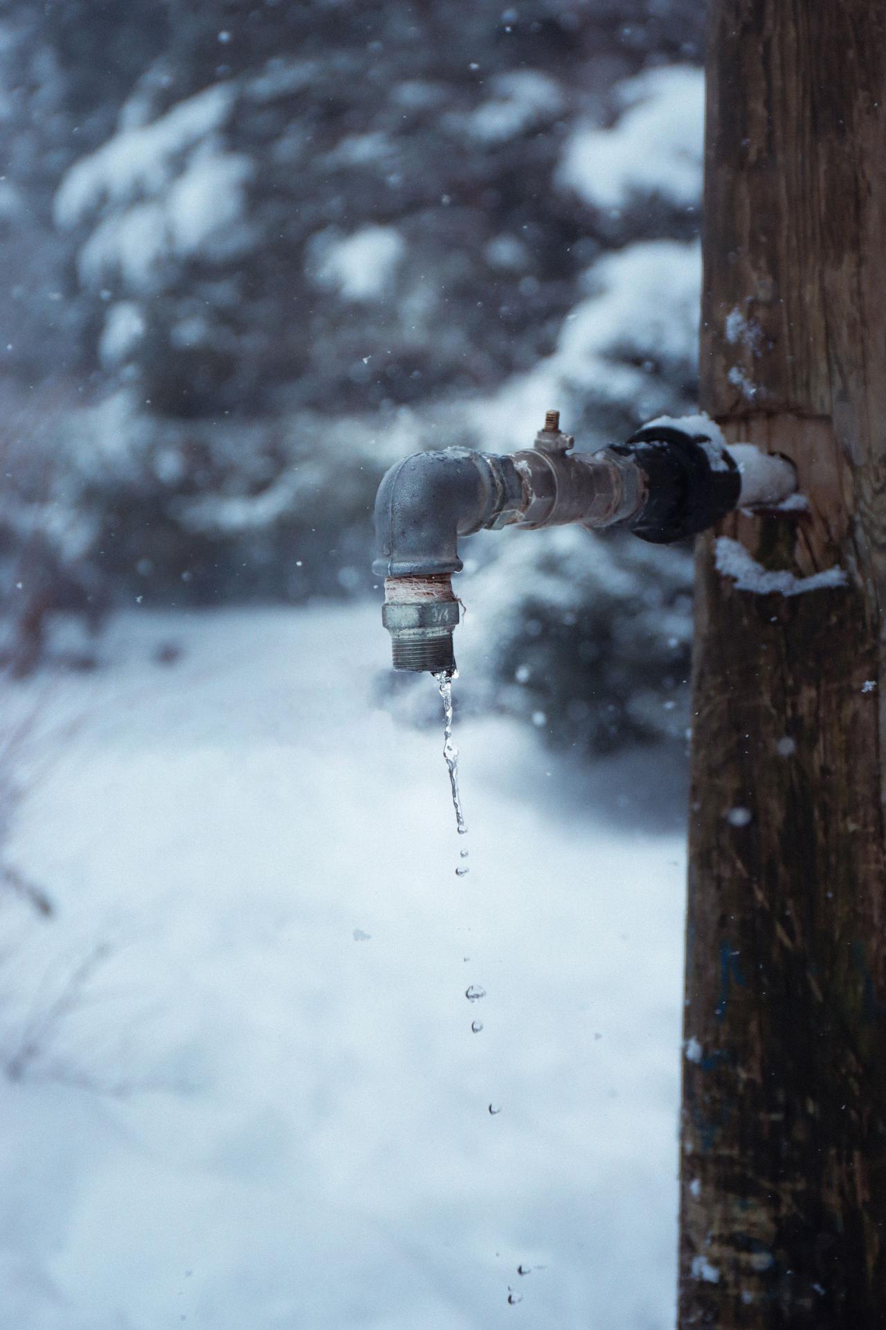 Outdoor faucet dripping in the snow during a hard freeze