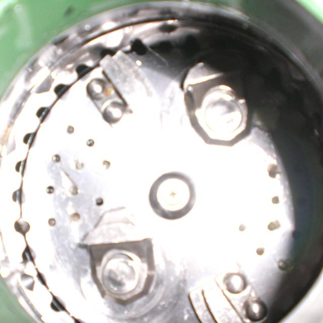 Looking down into a garbage disposal's grinding chamber, showing the metal turntable with two impeller lugs, small drain holes, and the grind ring