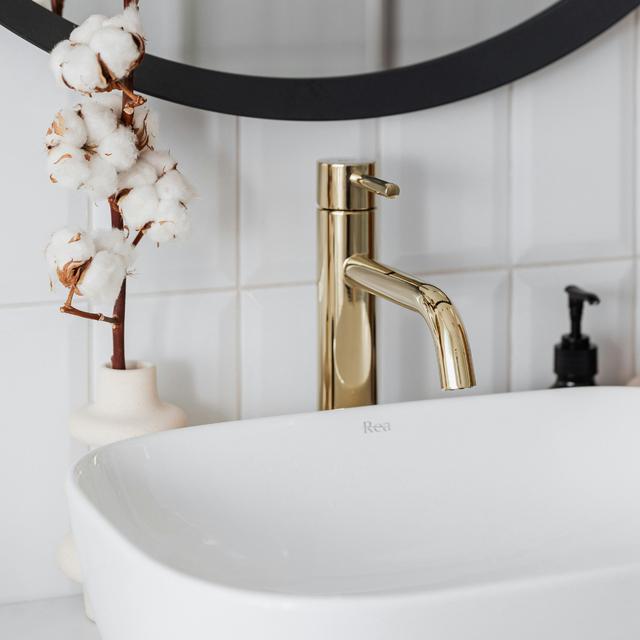 Brushed gold faucet over a white rectangular vessel sink in a bright bathroom