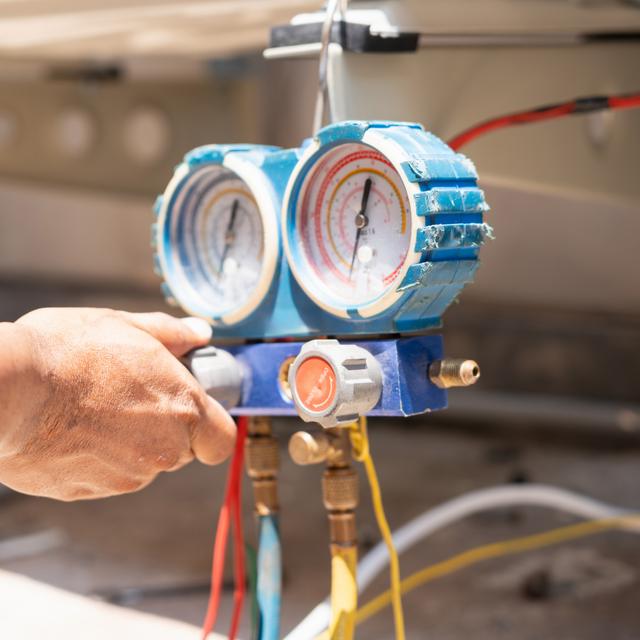 Technician's hand turning the valve on a blue refrigerant manifold gauge set
