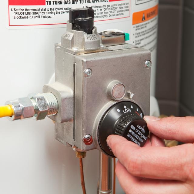 Hand turning the temperature dial on the gas control valve of a water heater