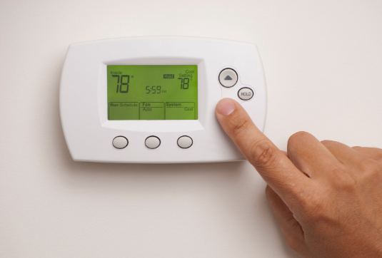 Hand adjusting a programmable thermostat with a green display reading 78 degrees