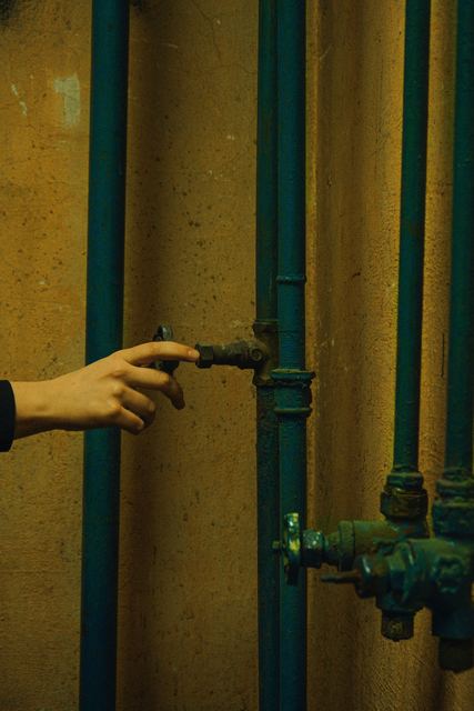 Hand reaching for a shutoff valve on a water pipe