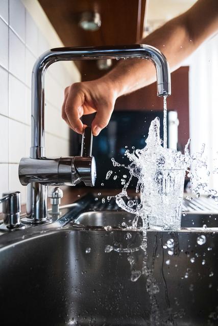 Hand turning on a kitchen faucet over a glass of water