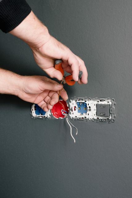 Hands working a wire connector at an open wall box