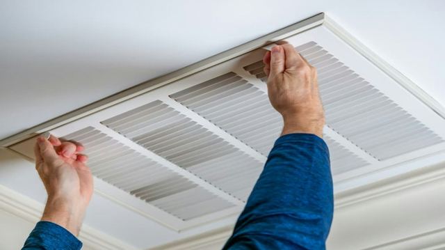 Hands removing a ceiling return air grille to service the ductwork