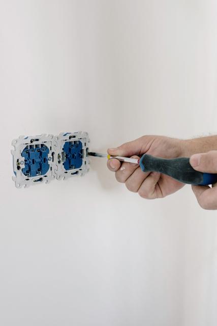 Hand using a screwdriver on the wiring inside an open wall box