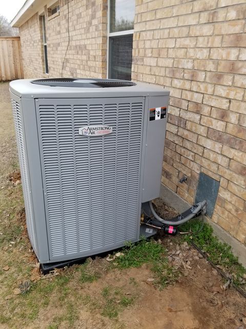 Newly installed air conditioning condenser on a pad beside the brick wall of a home, line set and disconnect in place