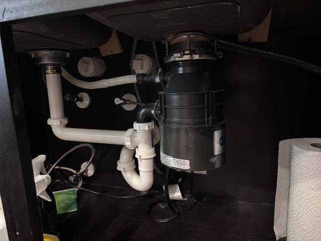 InSinkErator garbage disposal installed under a kitchen sink, connected to white PVC drain lines and a dishwasher hose