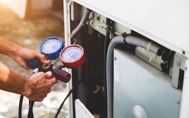 Hands holding manifold gauges hooked to an outdoor unit during a refrigerant check