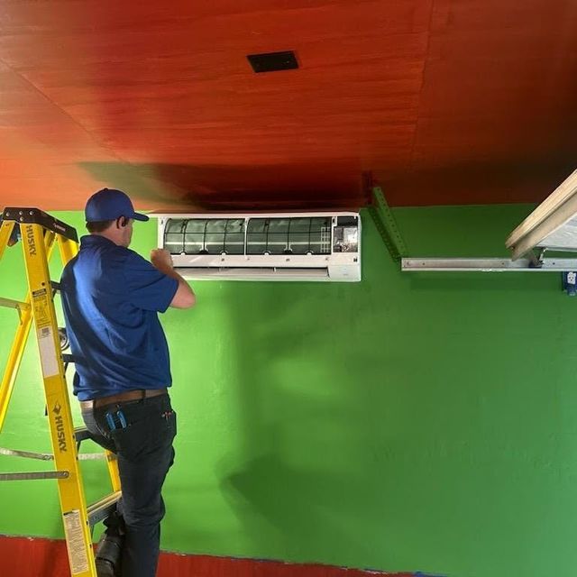 HMS technician on a ladder mounting a ductless mini split head on the wall