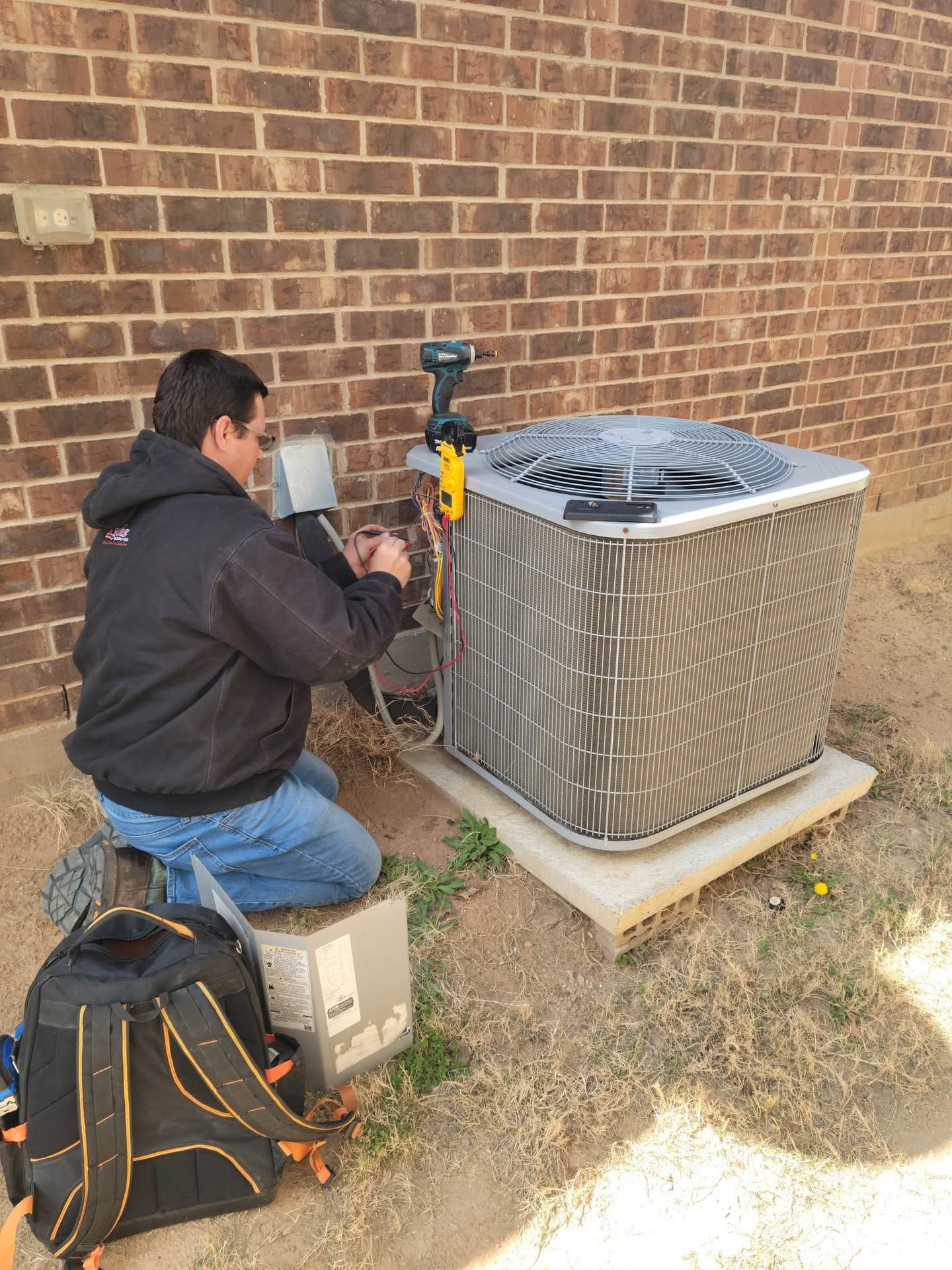 HMS technician working at the electrical disconnect beside an outdoor condenser at a brick home