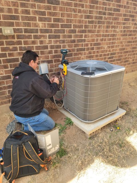 HMS technician kneeling at the electrical disconnect beside an outdoor condenser at a brick home