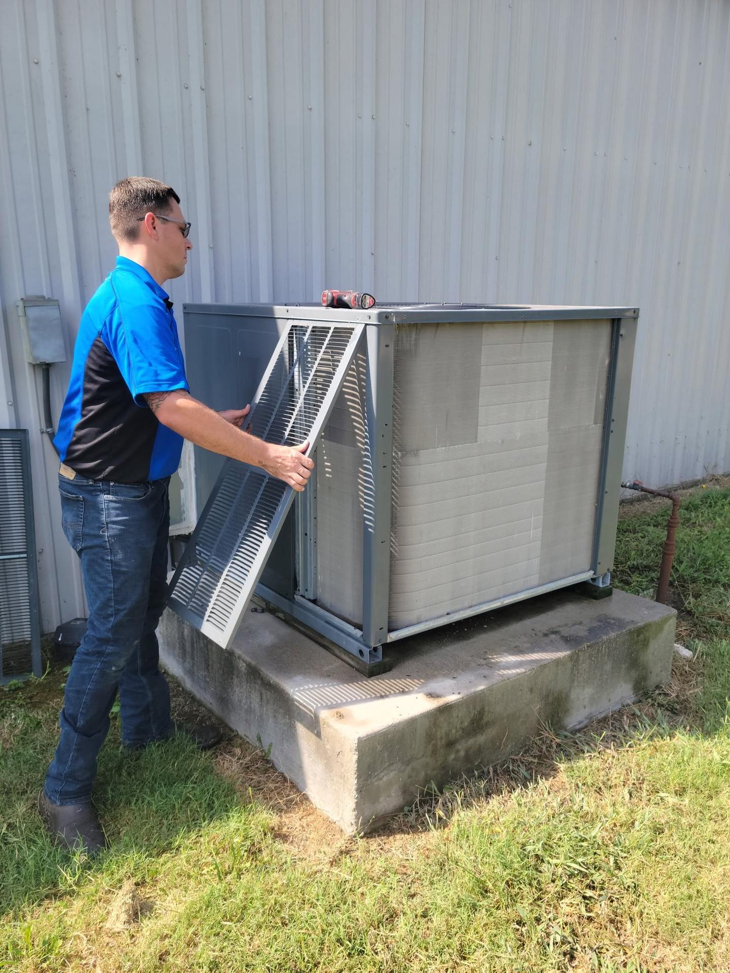 HMS technician in a company polo lifting the coil access panel off an outdoor air conditioning condenser