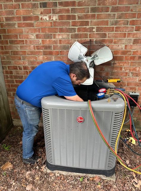 HMS technician leaning into an open outdoor air conditioning condenser with service gauges attached, working beside a brick home