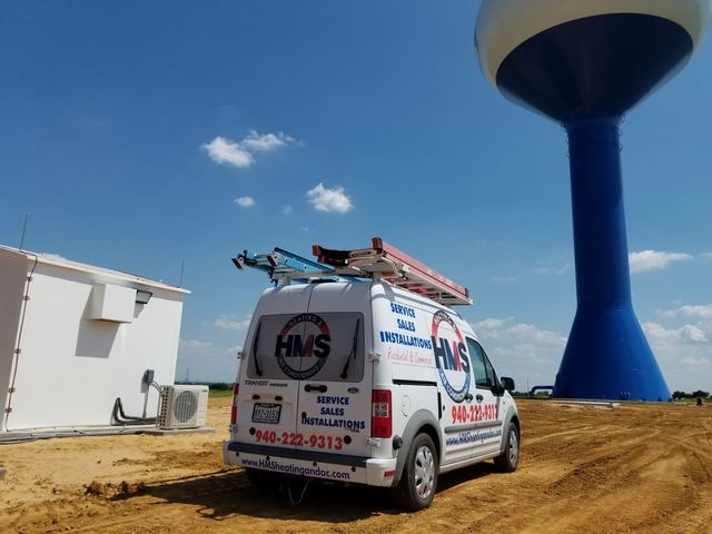 HMS service van parked on a rural job site beside a water tower