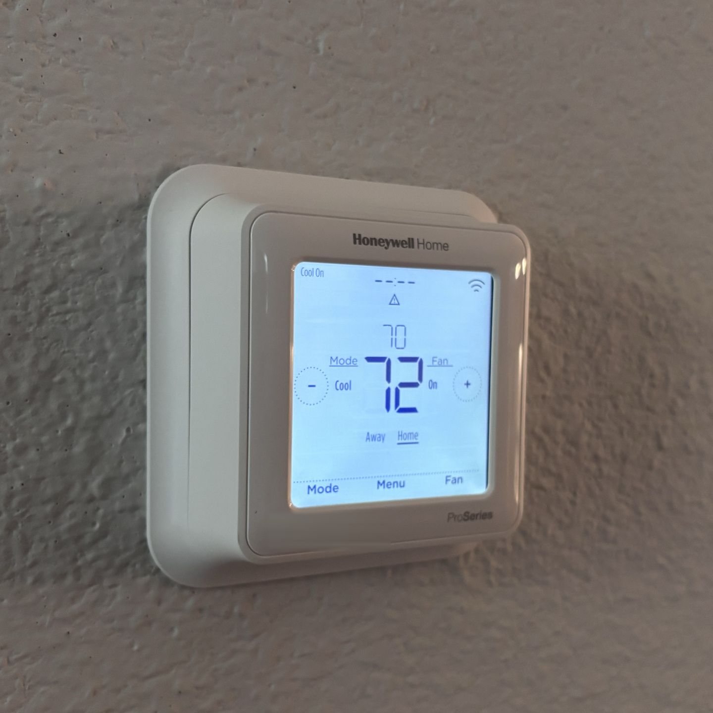 Honeywell Home ProSeries thermostat mounted on a textured wall, its screen set to cool at 72 degrees with the room at 70