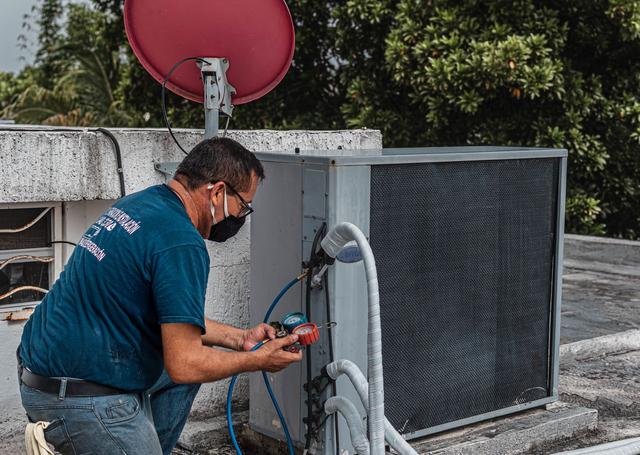 Technician reading manifold gauges at an open outdoor unit