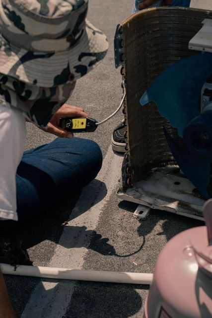 Technician crouched at an open condenser taking a meter reading