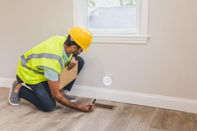 Worker with a clipboard kneeling to check a floor air register