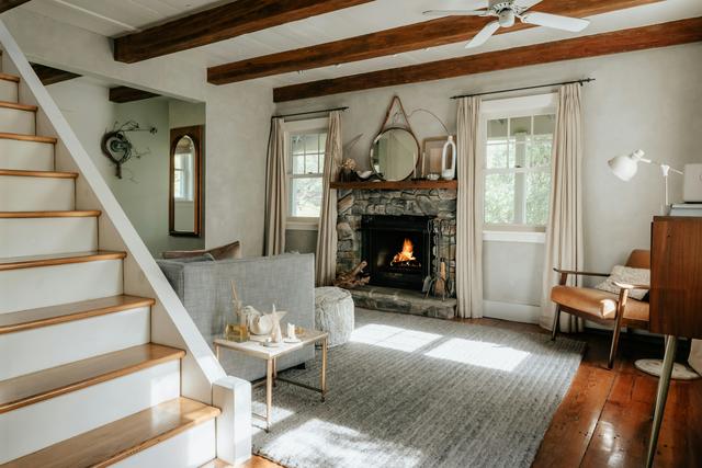 Sunlit living room with a lit stone fireplace beside the staircase