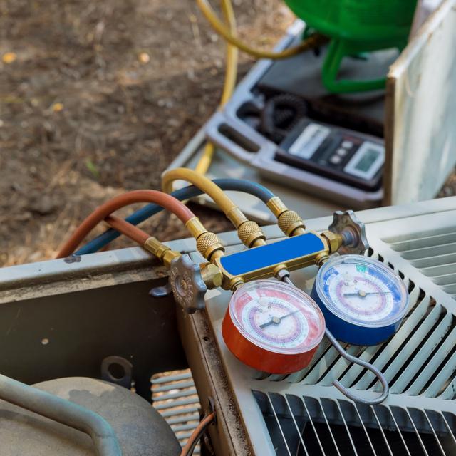 Refrigerant manifold gauges and hoses resting on top of an open outdoor AC condenser