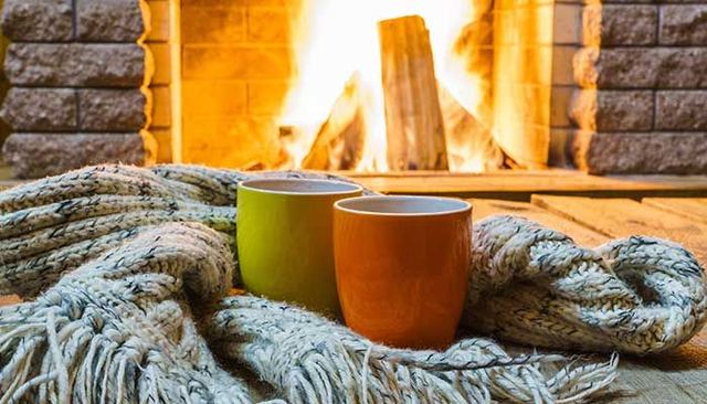 Two mugs resting on a knit blanket in front of a crackling fireplace