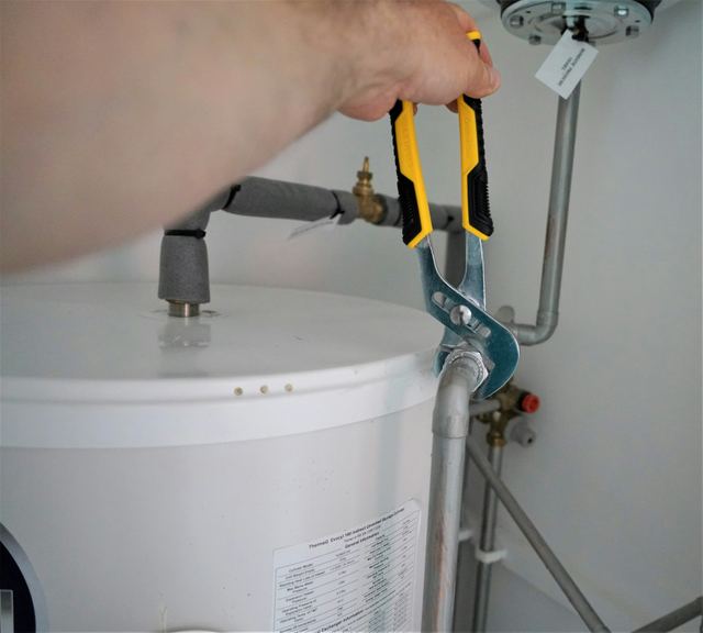 Hand using pliers on the fittings at the top of a water heater