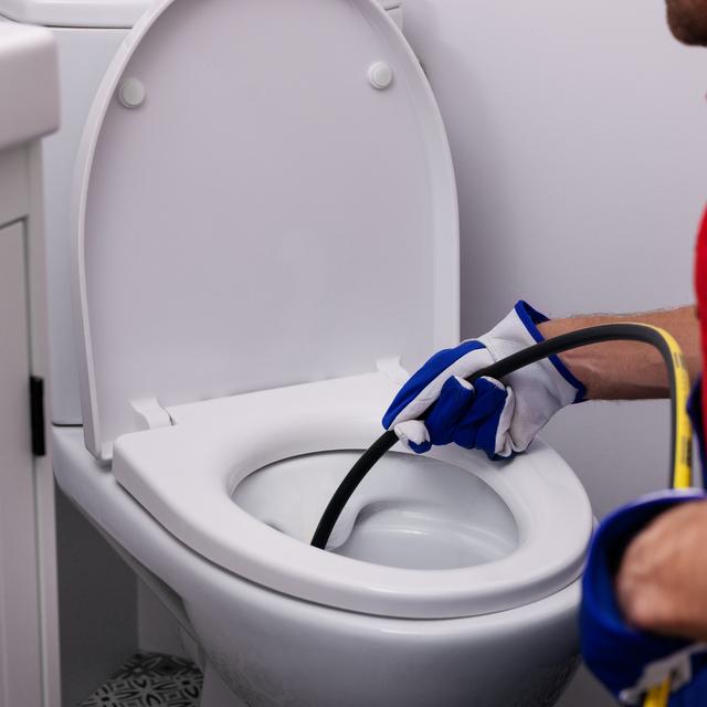 Gloved plumber running a drain auger cable into a toilet bowl