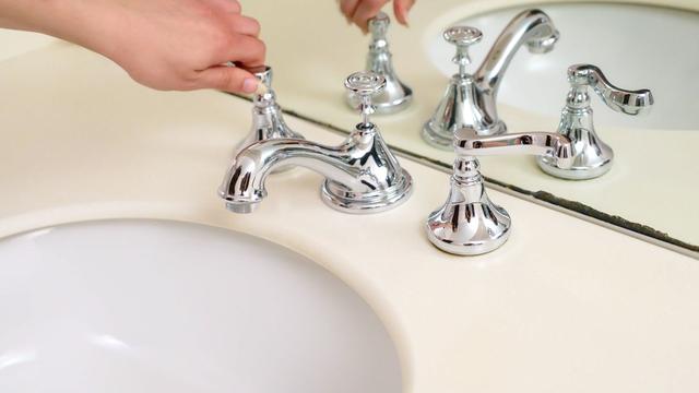 Hands working on a chrome faucet at a bathroom sink