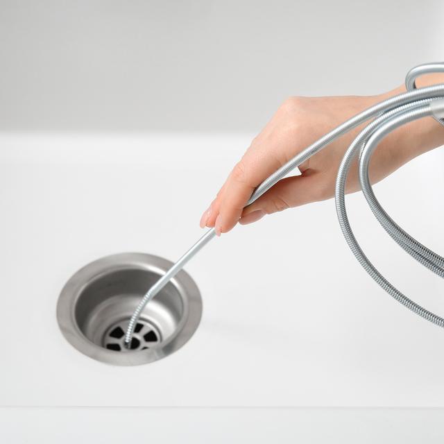 Hand feeding a drain snake into a white bathroom sink drain