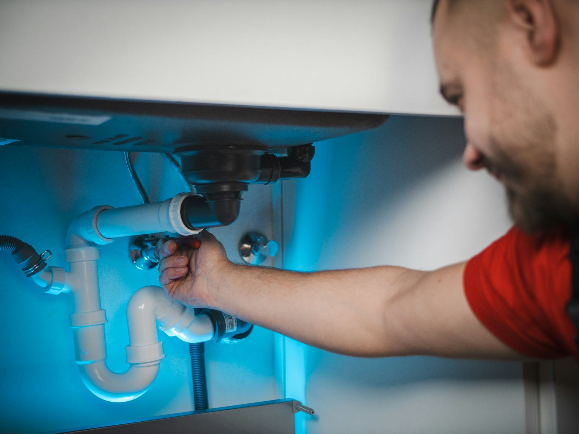 Plumber working under a sink to repair a leaking drain pipe