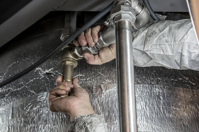 Hands turning a wrench on a threaded pipe joint