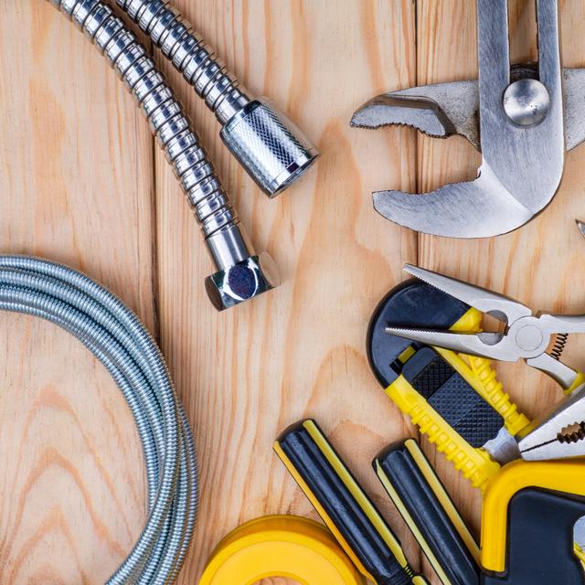 Adjustable wrench, pliers, screwdrivers, tape measure, and braided supply hoses laid out on a wood surface