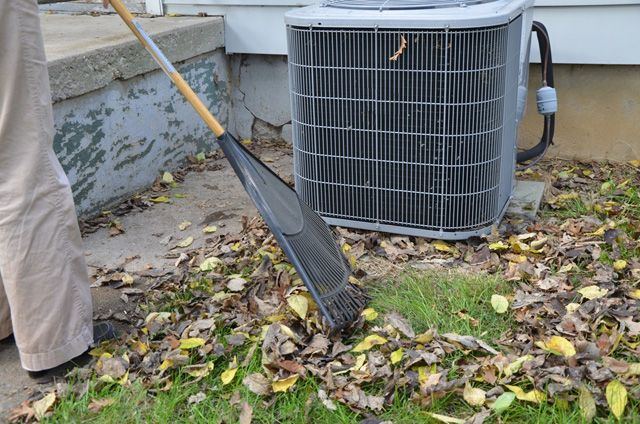 Rake clearing fallen leaves away from an outdoor air conditioner condenser
