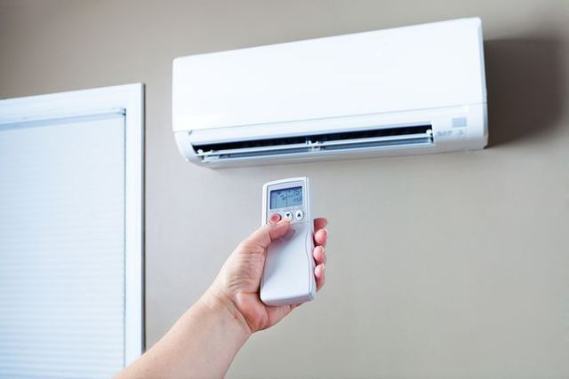 Hand pointing a remote control at a wall mounted ductless mini split unit