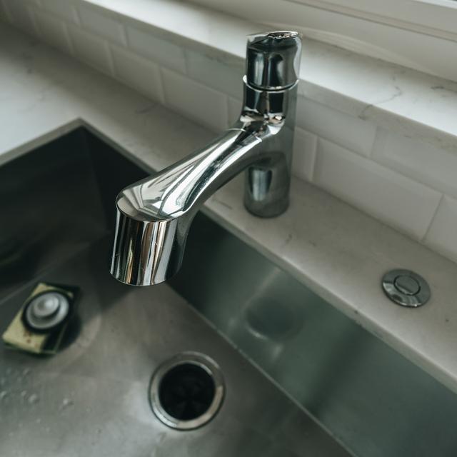Undermount stainless steel kitchen sink with a garbage disposal drain opening, a disposal stopper on a sponge, and a countertop air switch button beside the faucet