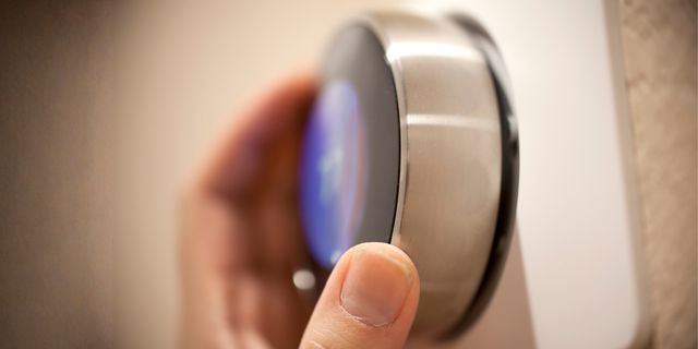 Hand turning the dial of a round smart thermostat on a wall