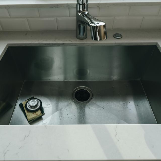 Front view of a single-bowl stainless steel kitchen sink with a centered garbage disposal drain, a disposal stopper on a sponge, and a chrome faucet