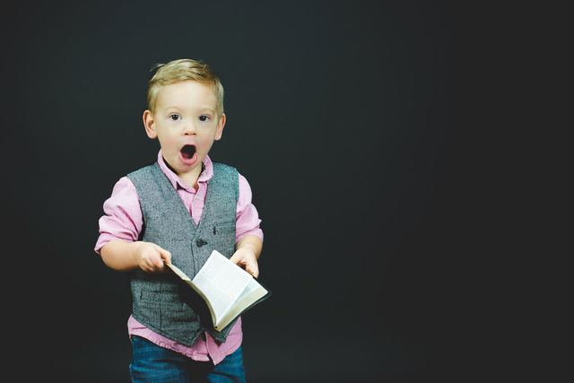 Surprised young boy with his mouth open, holding an open book
