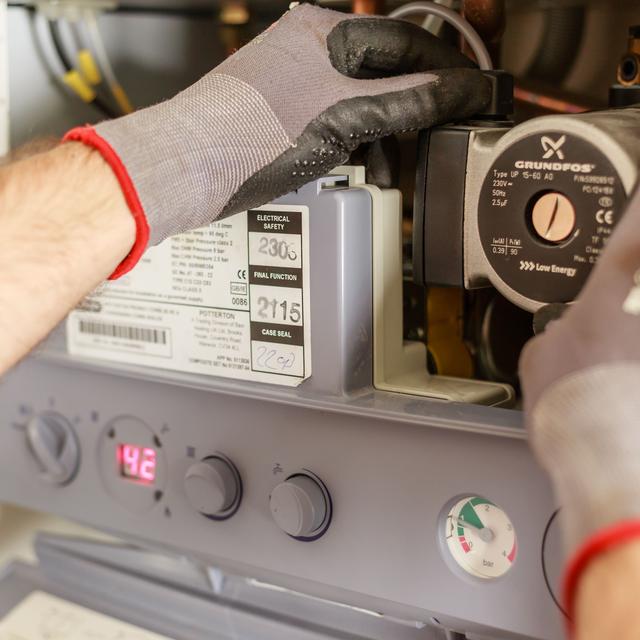 Gloved hands checking the controls inside an open heating unit with a digital readout
